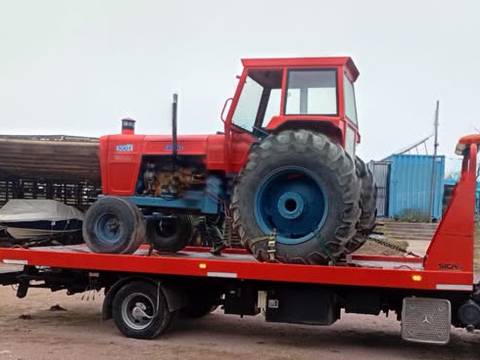 Tractor rojo con cabina, sobre la plataforma de una grúa