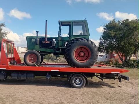 Tractor antiguo verde con cabina, sobre la plataforma de una grúa